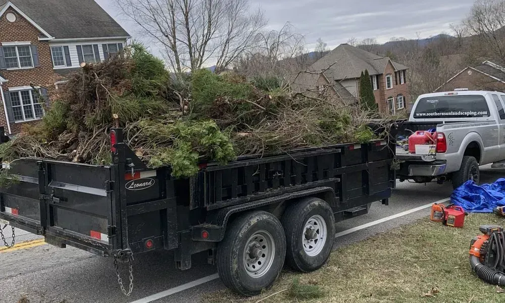 A black loader towed by a car carrying torn up sand and removed grass after underbrush removal and