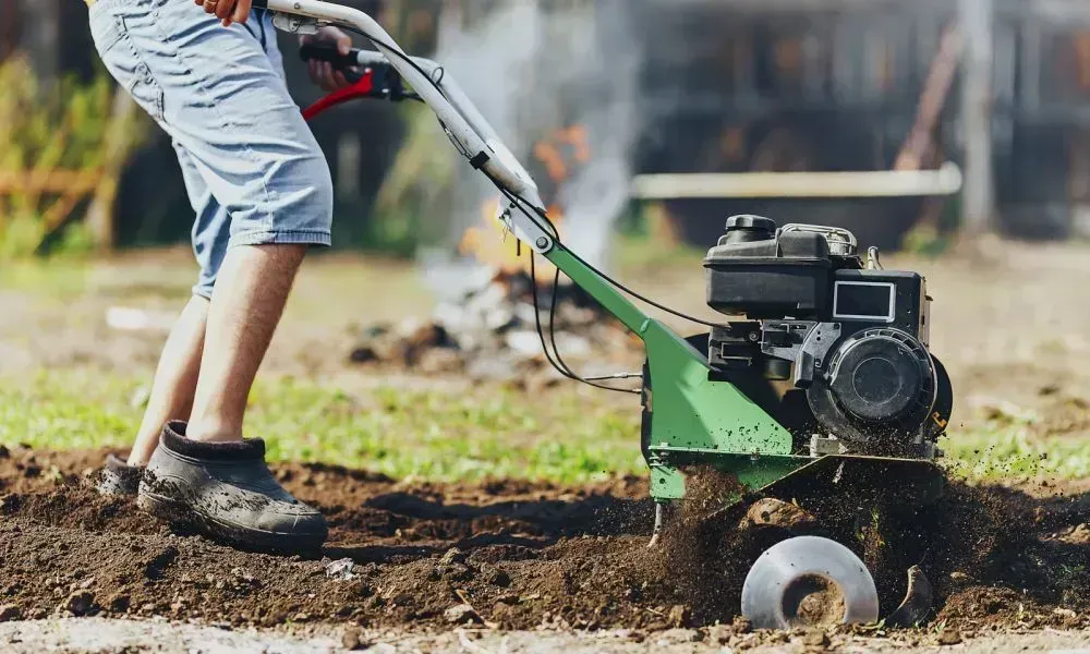 Closeup shot of a man using the manual stump grinder for tree stump removal from a lawn area