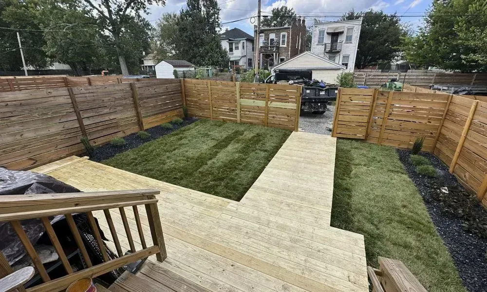 Long shot of garden outside a house with wooden pathways and a wooden boundary wall showcasing