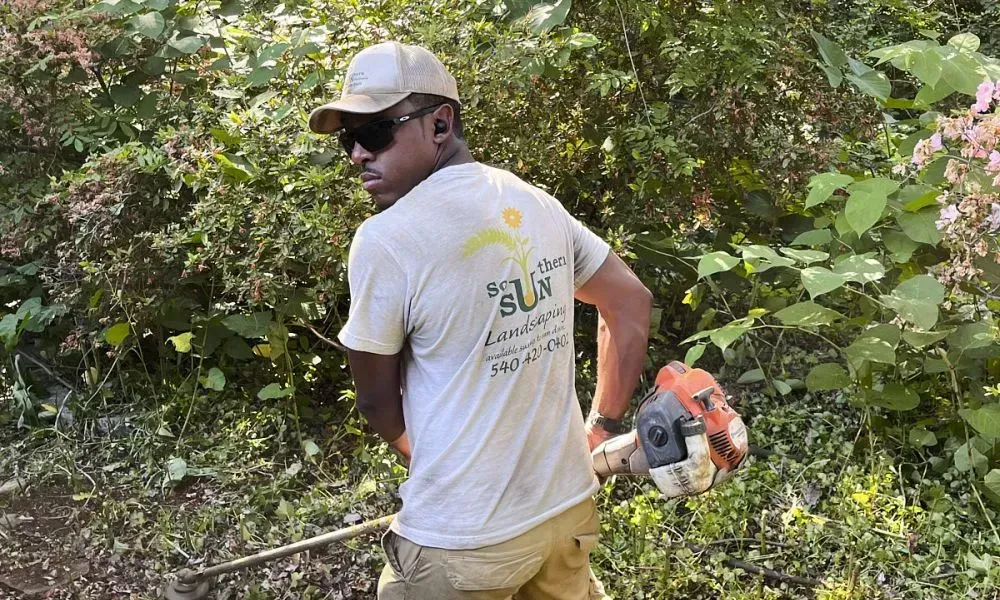 Professional using a string trimmer for vegetation removal on a lawn like area with sparse or dead