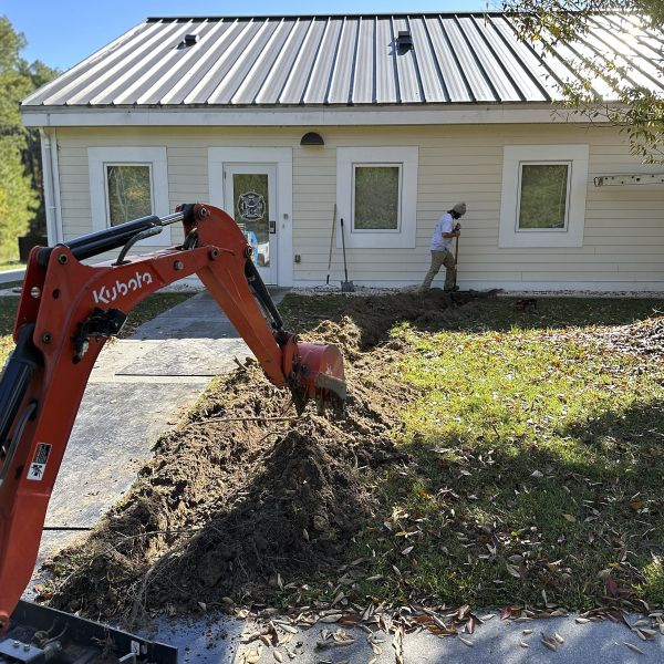 An Excavator In The Lawn Outside A House Digging A Trench For Proper Landscape Grading And Yard Leveling